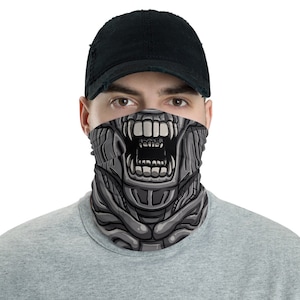 May include: A gray and black face mask with a graphic of a creature with a large open mouth and sharp teeth. The mask is worn by a person with a black baseball cap.