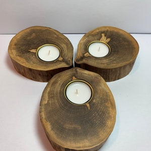 May include: Three wooden candle holders, each with a natural wood grain finish and a small, round, gold-rimmed candle holder in the center. The candle holders are arranged in a triangular shape.