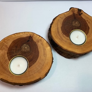 May include: Two wooden candle holders with a natural wood finish. Each holder has a round, recessed area for a tea light candle.