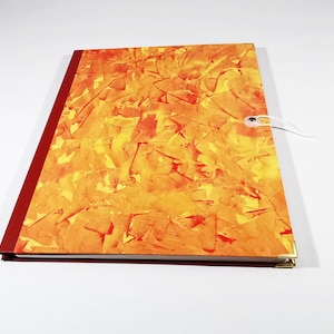 Könnte beinhalten: Ein rotes und goldenes Journal mit einem strukturierten Einband und einem weißen Kordelverschluss. Das Journal hat ein goldenes Eckdetail.