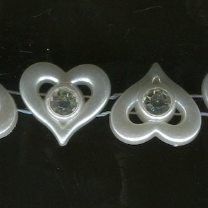 May include: A delicate necklace featuring a series of white heart-shaped charms, each adorned with a sparkling, round, clear gemstone. The hearts are strung together on a thin, nearly invisible strand, creating a romantic and elegant accessory.