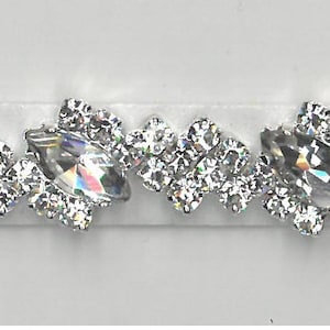 Op de afbeelding: Een decoratieve sierband met heldere, sprankelende strass-steentjes in een bloemmotief. De band heeft een centrale rij marquise-vormige stenen, omringd door kleinere, ronde strass-steentjes, alles op een witte achtergrond. Ideaal voor het verfraaien van kleding of accessoires.