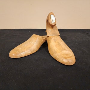 May include: A pair of wooden shoe trees with a label that reads "Schuh-hilfe". The shoe trees are brown and have a smooth finish.