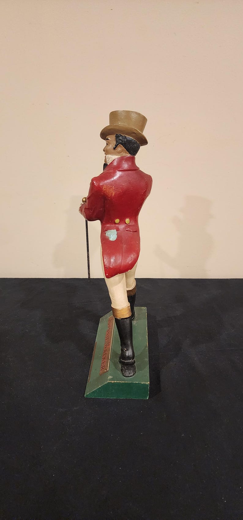 Puede incluir: Figura vintage de un caballero con abrigo rojo, botas negras y sombrero de copa, sosteniendo un bast&oacute;n. La figura se alza sobre una base verde con texto. Una pieza decorativa cl&aacute;sica.