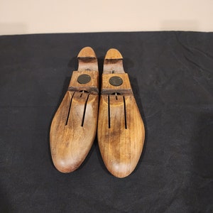 May include: A pair of wooden shoe trees with a brown finish. The shoe trees have a round shape and are designed to help maintain the shape of shoes.