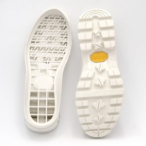 May include: A pair of white shoe soles, one with a waffle-like pattern and the other with a textured tread pattern. The sole with the tread pattern has a yellow "Vibram" logo.