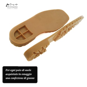 Puede incluir: Dos suelas de zapatos de cuero marrón, una con una superficie lisa y la otra con un patrón de banda de rodadura texturizado. El texto "Per ogni paio di suole acquistate in omaggio una confezione di grasso" está impreso debajo de las suelas.