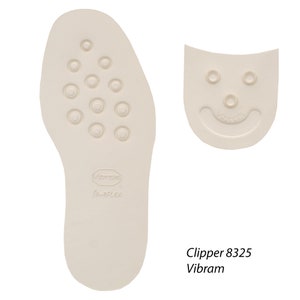 Può includere: Un paio di solette per scarpe bianche con una superficie testurizzata e un logo Vibram. Le solette sono progettate per un maggiore comfort e supporto. Il testo "Clipper 8325 Vibram" è stampato sotto le solette.