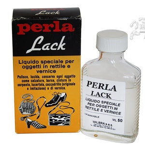 Può includere: Una bottiglia di vetro trasparente con un tappo bianco contenente un liquido chiamato "Perla Lack". L'etichetta della bottiglia riporta "Liquido Speciale per Oggetti in Rettile e Vernice" e "Wilbra S.a.s.". La bottiglia è appoggiata su una superficie bianca accanto a una scatola gialla e nera con lo stesso nome e descrizione del prodotto.
