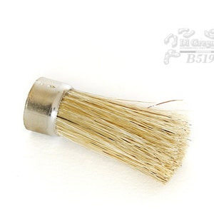 Könnte beinhalten: Eine kleine, runde, silberfarbene Bürste mit einem Bürstenkopf aus Naturborsten. Die Bürste hat einen Durchmesser von etwa 2,5 cm und ist 3,8 cm lang.