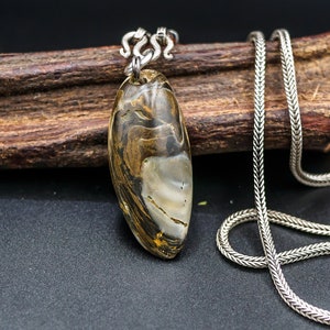 Può includere: Una collana con catena d'argento con un ciondolo in agata marrone e bianco. Il ciondolo è di forma ovale e presenta un motivo naturale e organico.