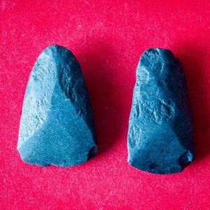 May include: Two dark blue, smooth, stone tools with a pointed tip. The tools are displayed on a red velvet surface.