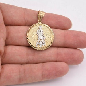May include: Gold pendant featuring a detailed image of a saint with a staff and two dogs. The pendant is round and has a textured edge.