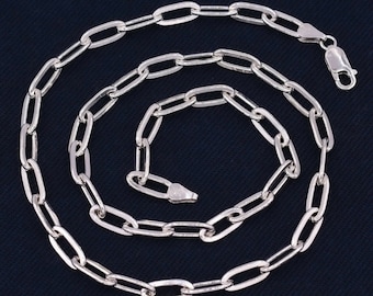 Può includere: Una collana a catena d'argento con un classico design a maglie ovali. La catena è disposta a spirale su uno sfondo blu scuro.