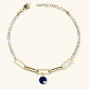May include: Gold chain bracelet with a blue enamel charm and a single clear crystal. The bracelet is adorned with clear crystals.