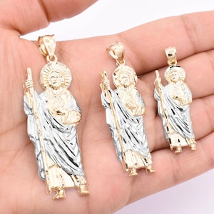 May include: Three gold and silver pendants featuring a religious figure with a staff. The pendants are different sizes and are displayed on a hand.