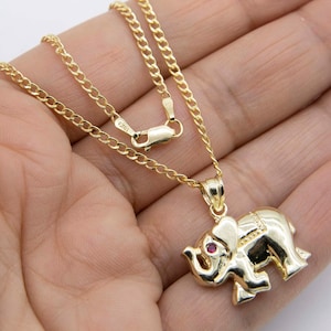 Op de afbeelding: Een gouden ketting met een gouden olifant hanger met een rode edelsteen oog. De ketting is van het curb-type.
