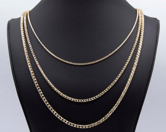May include: Three gold chains of different widths and lengths on a black display stand. The chains are made of a combination of yellow and white gold.