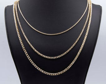 May include: Three gold chains of different widths and lengths on a black display stand. The chains are made of a combination of yellow and white gold.
