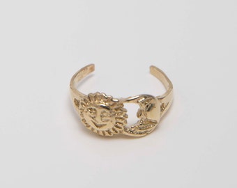 May include: A gold toe ring with a sun and moon design. The sun has a smiling face.