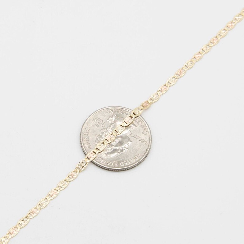 K&ouml;nnte beinhalten: Eine goldene Kettenkette mit einem zarten, gemusterten Design. Die Kette liegt zur Gr&ouml;&szlig;envergleich auf einer US-amerikanischen 25-Cent-M&uuml;nze.