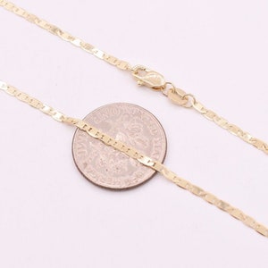 May include: A gold chain necklace with a mariner link design. The chain is laid out on a white surface next to a US quarter.