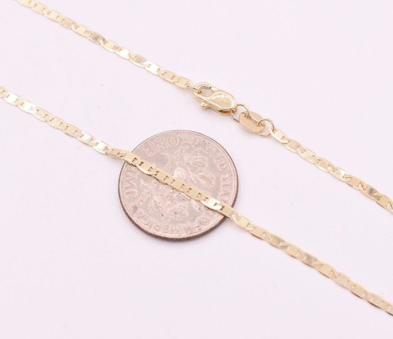 May include: A gold chain necklace with a mariner link design. The chain is laid out on a white surface next to a US quarter.