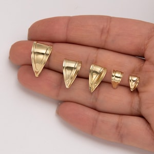May include: A collection of five gold-colored pendant bails in varying sizes. Each bail has a triangular shape with a decorative band near the top. The bails are displayed against a neutral background.