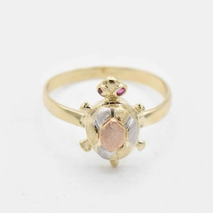 May include: A gold ring with a three-toned turtle design. The turtle's shell is made of yellow, white, and rose gold. The turtle has two small red gemstones for eyes.