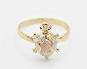 Op de afbeelding: Een gouden ring met een driekleurig schildpadontwerp. De schildpad heeft een schild van geel, wit en roségoud. De schildpad heeft twee kleine rode edelstenen voor ogen.
