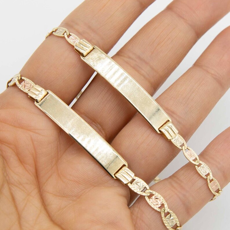 May include: Two gold ID bracelets with a textured finish. The bracelets are linked together and feature a chain with a diamond pattern.
