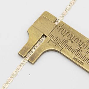 K&ouml;nnte beinhalten: Nahaufnahme einer goldenen Kette mit einem Diamantenmuster, die mit einer Schieblehre gemessen wird. Die Schieblehre zeigt "METER" an und hat Markierungen in Millimetern.