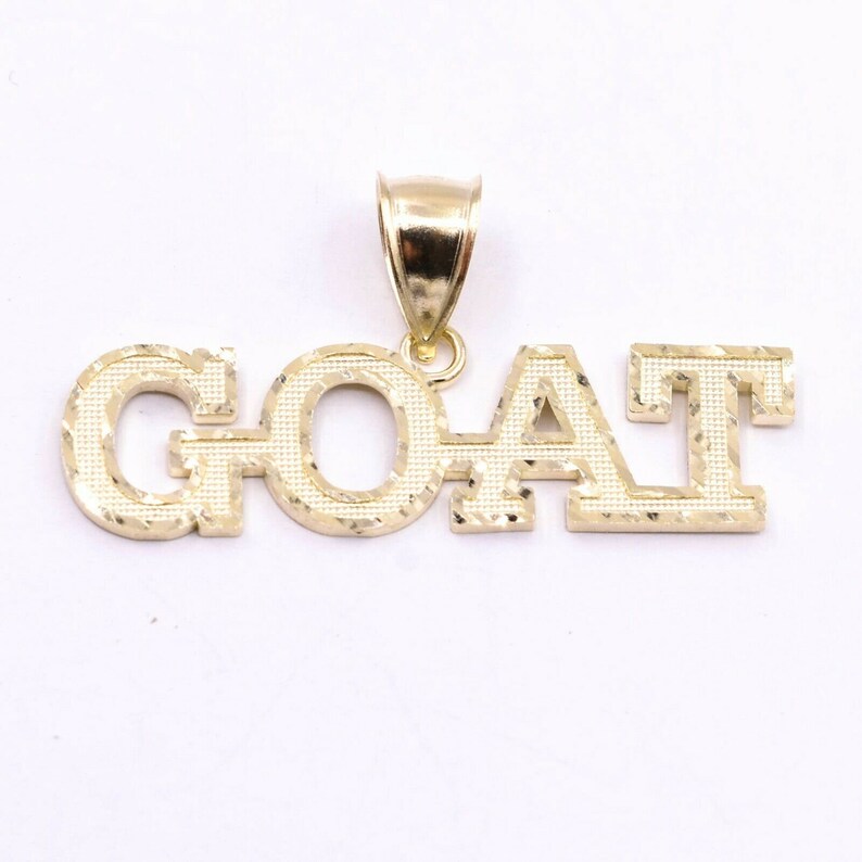 May include: Gold pendant necklace with the word "GOAT" in a diamond-cut style.