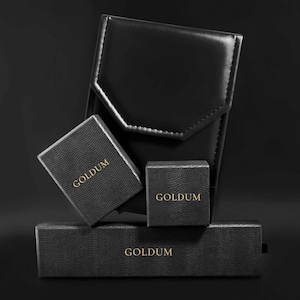 May include: Four black boxes with the word "GOLDUM" printed in gold lettering. The boxes are stacked on top of each other.
