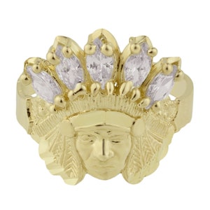 May include: A gold ring featuring a detailed depiction of an indigenous person's face wearing a headdress adorned with clear marquise-shaped stones.