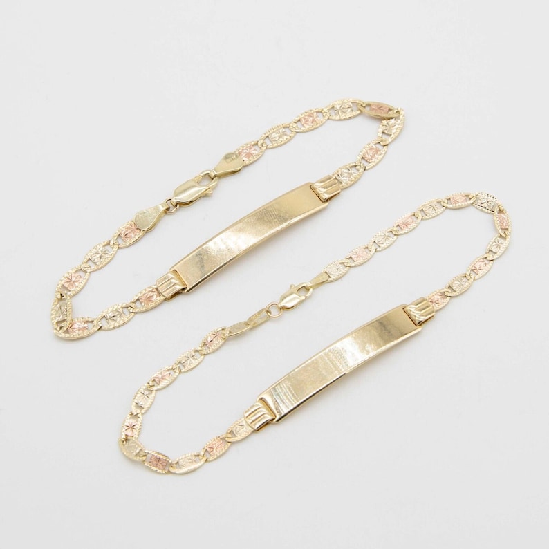May include: Two gold bracelets with a delicate, patterned design. Each bracelet features a flat, rectangular tag.