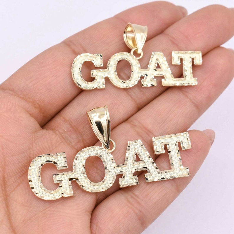 May include: Two gold pendants with the word "GOAT" spelled out in block letters. The letters have a diamond-cut texture.