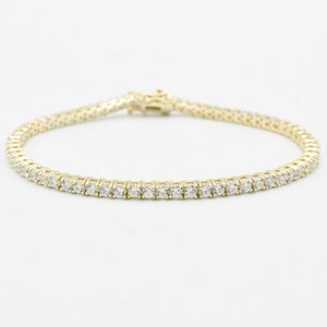May include: A gold tennis bracelet with a row of clear round stones.