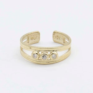 May include: Gold toe ring with three clear round stones set in a double band design.