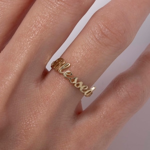 Könnte beinhalten: Goldring mit dem Wort "blessed" in Kursivschrift.