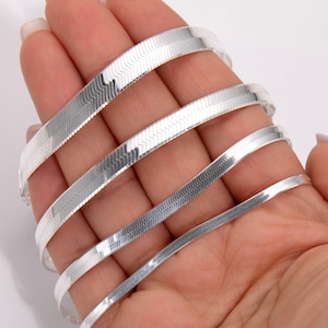 May include: Four silver snake chains of varying widths, displayed on a hand.