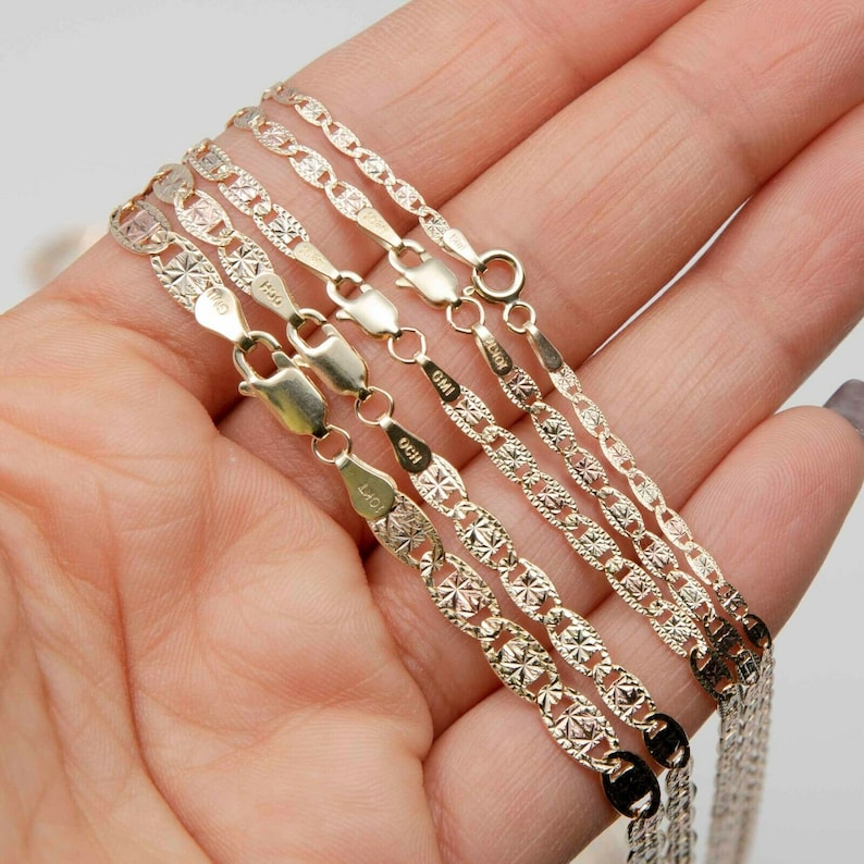 May include: Five gold chains of different widths and styles, all with a delicate, patterned design. The chains are arranged in a fan shape, with the widest chain at the top and the narrowest chain at the bottom.