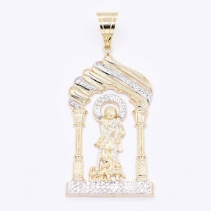 May include: A gold and white pendant featuring a religious figure standing in an archway with two pillars. The pendant is detailed with a textured design and small stones.