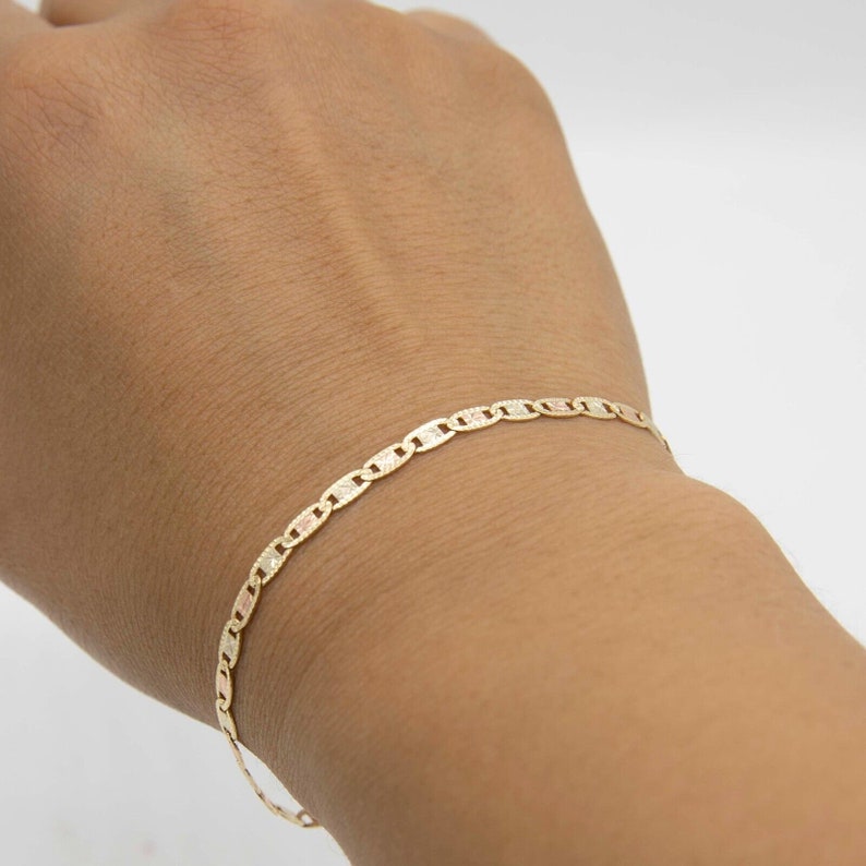 Puede incluir: Un brazalete de cadena de oro con un dise&ntilde;o de eslab&oacute;n marinero. El brazalete est&aacute; en la mu&ntilde;eca de una persona.