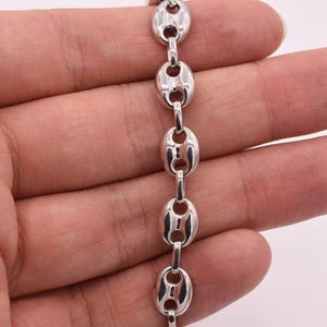 May include: A silver-toned chain bracelet featuring a series of polished, oval-shaped links. Each link has a distinct center bar design, creating a uniform and repeating pattern throughout the length of the metallic jewelry piece.