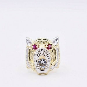 Op de afbeelding: Een gouden en zilveren ring met een tijgerkop, met rode robijnogen en een heldere diamant in het midden.