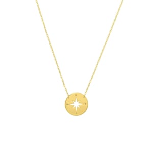 Puede incluir: Un collar de oro con un colgante de brújula. El colgante es un círculo con una rosa de los vientos recortada en el centro. La rosa de los vientos tiene las letras N, S, E y W alrededor del exterior.