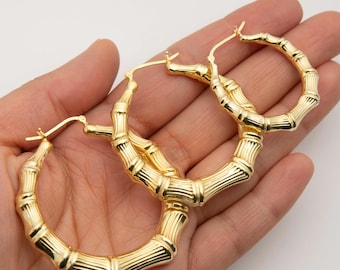 May include: A pair of gold-toned hoop earrings featuring a textured bamboo-inspired design. The circular earrings have a polished, reflective finish and a hinged post closure mechanism at the top, showcasing a segmented, organic stalk appearance.