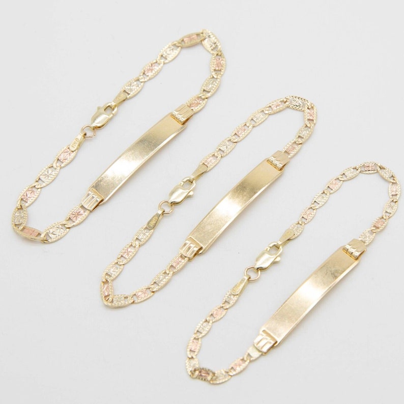 May include: Three gold bracelets with a delicate, patterned chain and a rectangular nameplate charm. The nameplates are blank and ready to be engraved.