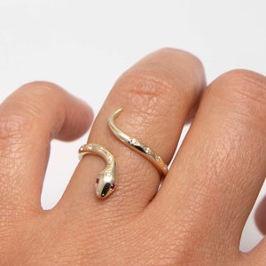 Op de afbeelding: Een gouden slangenring met een robijnoog en heldere stenen op het lichaam.